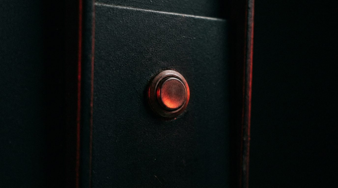 A single glowing red push-button isolated on a dark worn panel, dramatic low-key lighting, shallow depth of field, film grain