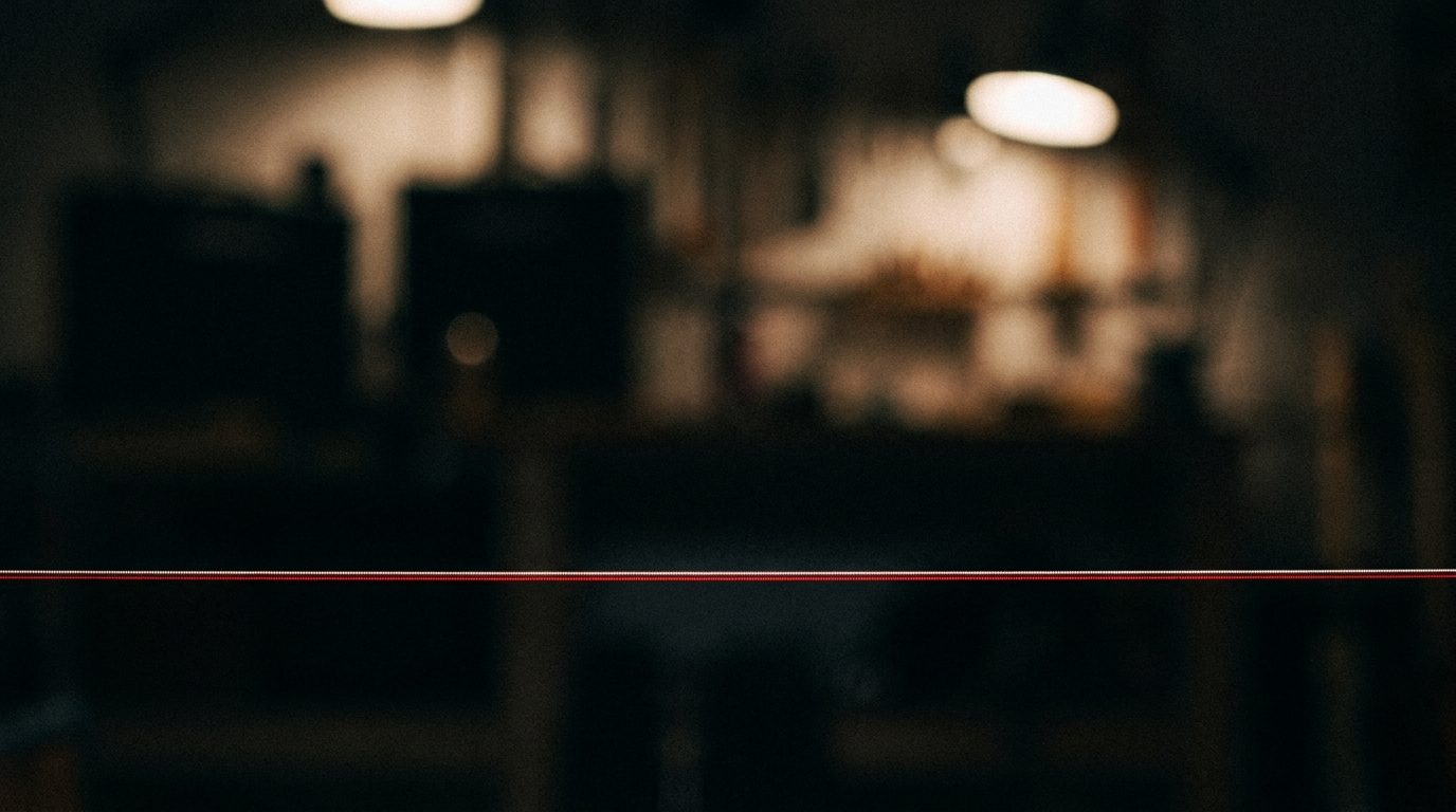 A single sharp red laser line projected across a dark workbench, with a blurred diffuse light in the background